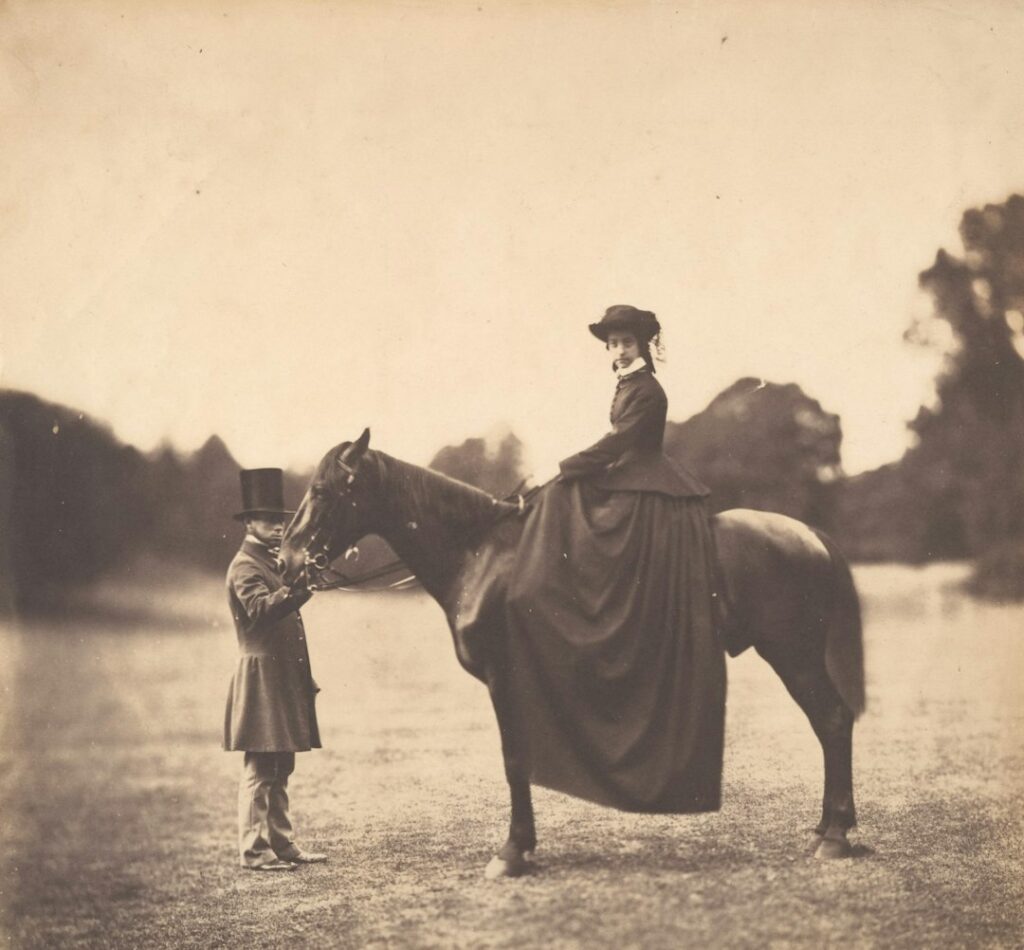 A woman on horseback with a man adjusting the bridle.
