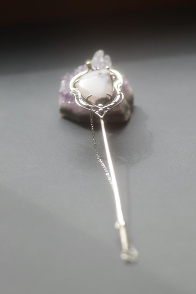 a silver brooch with a white flower on it
