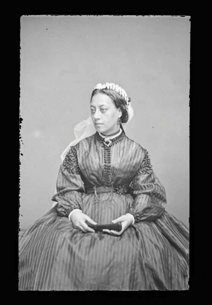 Woman in striped dress and headpiece holding an object.